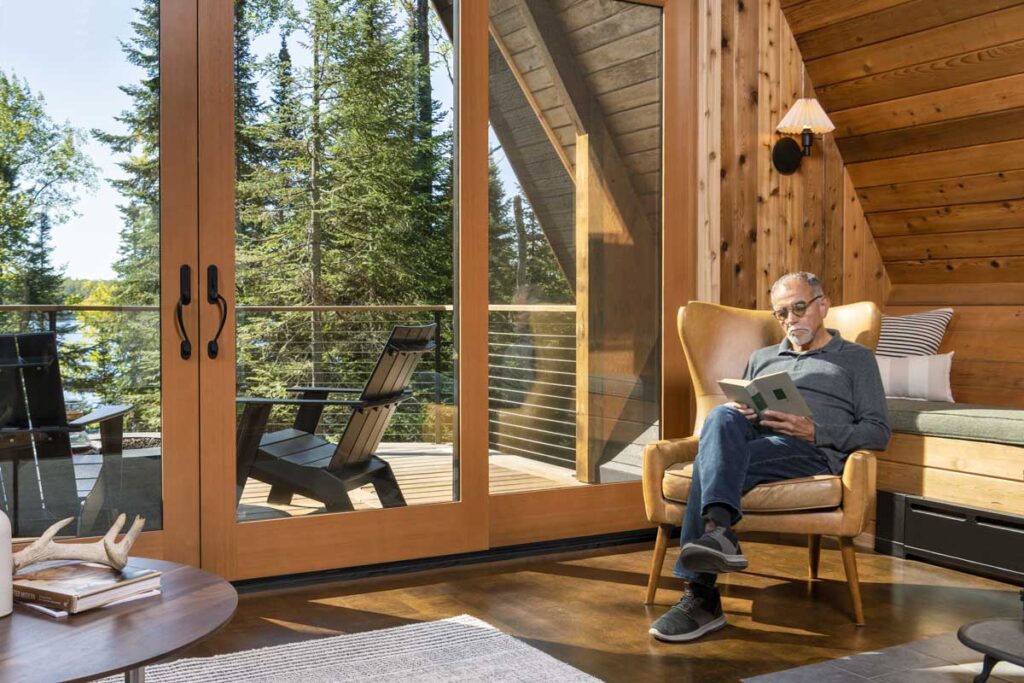 A man sitting in a chair by a window, reading a book.